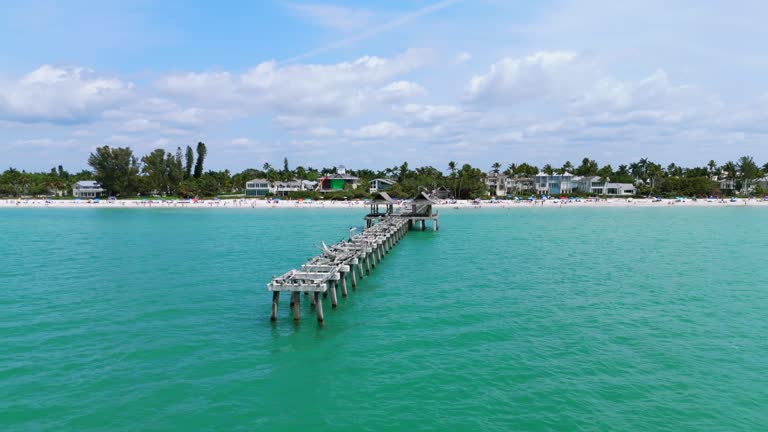 Serene view of Naples, Florida surrounded by calm and clear turquoise waters under bright blue sky. Partially constructed or damaged pier with visible concrete supports