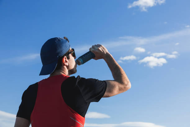 A trail runner drinking in a bottle against a blue sky, embodying a spirit of freedom, achievement, and healthy lifestyle concept.