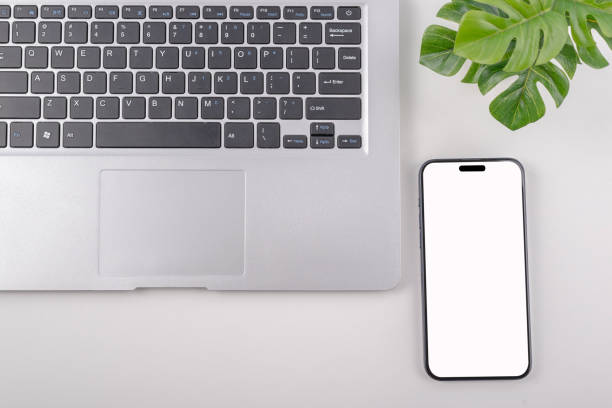 istock Modern white office desk table with laptop computer, smartphone with black screen over a notebook and cup of coffee. Top view with copy space. 2150409683