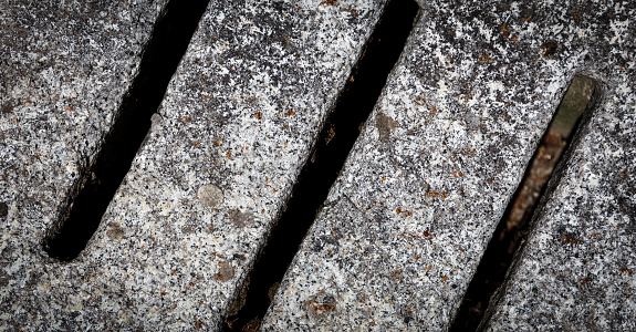 Close-up full frame shot of concrete gray textured sewer drain cover with parallel gaps