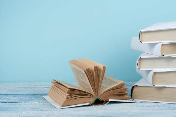 istock Book stacking. Open book, hardback books on wooden table and blue background. Back to school. Copy space for text. 2150412312
