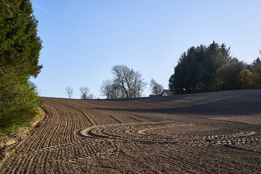 Scenic tranquil of plowed landscape with tire tracks at organic farm against clear sky during sunny day