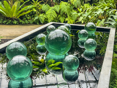 Glass spheres of various sizes on the reflective surface of a raised pool in a tropical garden conservatory, for motifs of arrangement, interrelation, contemplation. Light digital oil-painting effect.