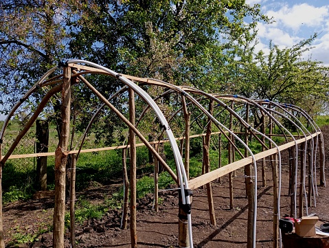A frame made of improvised materials of a home-made greenhouse. Construction of a greenhouse from wood. the topic of growing vegetables in greenhouses.