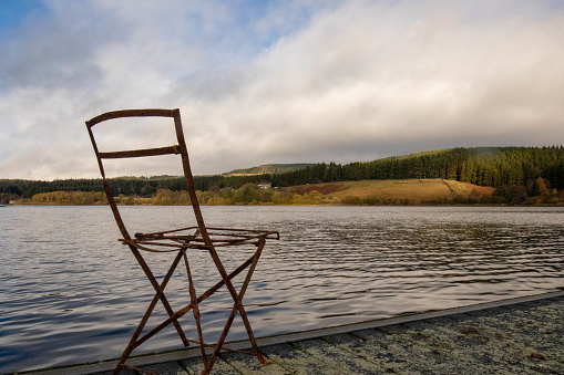 Rusty abandoned chair on jetty by Kielder lake on a cloudy day