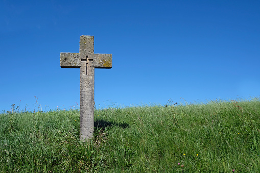 Cross made out of stone on a green grass field with the blue sky in the background