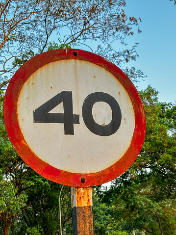 A rusted, old, and worn out sign with the speed limit 40km/hr on it. The sign is located in a forested area
