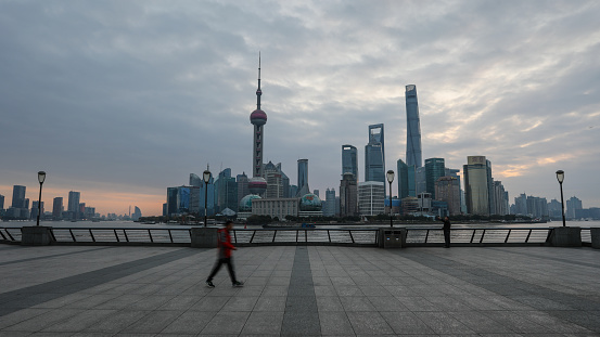 Shanghai, China - 12 02 2017: Commuters and tourist are walking on The Bund waterfront promenade. The Bund is a waterfront area view to Shanghai China modern skyscrapers skyline urban city.