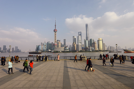Shanghai, China - 12 01 2017: Commuters and tourist are walking on The Bund waterfront promenade. The Bund or Waitan is a waterfront area view to Shanghai China modern skyscrapers skyline urban city.