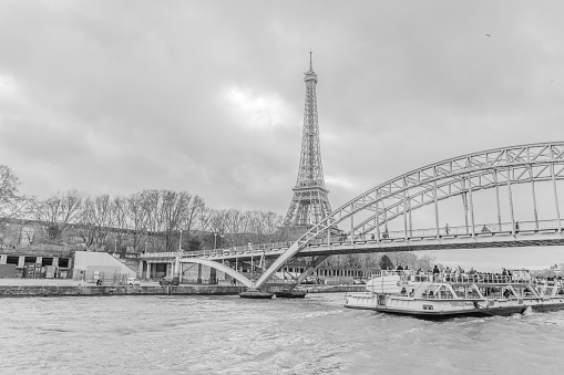 Paris, France - December 29, 2023:  A Seine River cruise boat passed underneath Passerelle Debilly with Eiffel Tower in the background as viewed from another cruise boat on a gloomy day.  HDR encoded