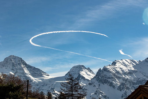 Curved Chemtrail above snowy mountains Swiss Alps Switzerland