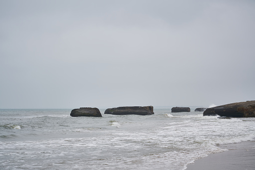 Waves splashing on abandoned Atlantic wall bunkers in seascape against cloudy sky at Løkken, Jutland, Denmark