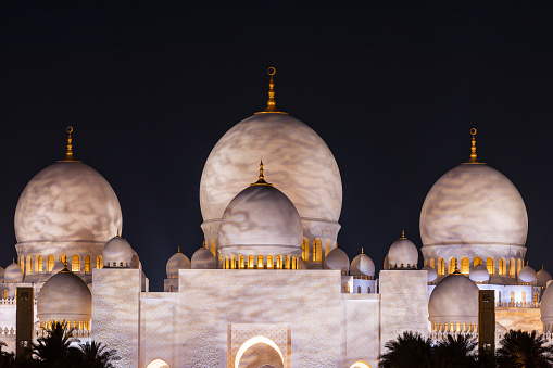 Abu Dhabi, UAE - April 23, 2024: Glowing domes and illuminated arches and of Sheikh Zayed Grand Mosque at night