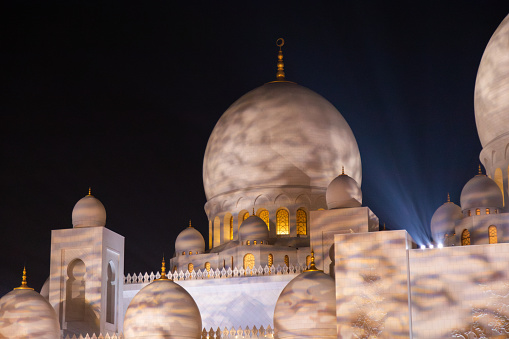 Abu Dhabi, UAE - April 23, 2024: Domes of the Sheikh Zayed Grand Mosque, with lights streaming through the darkness