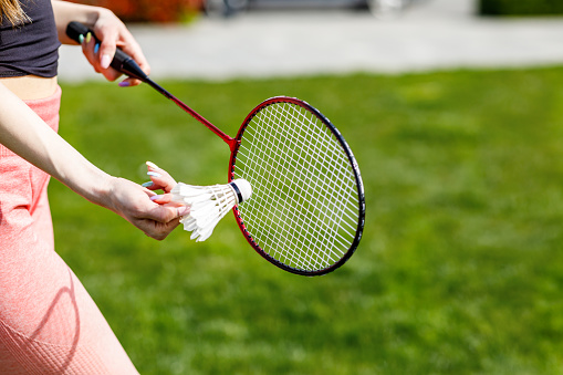 A Woman in Public Park is Playing Badminton While Holding a Racket and Shuttlecock.