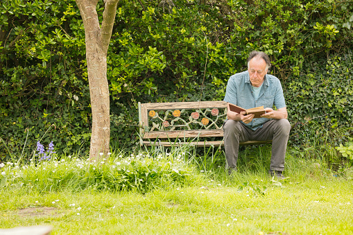 Retiree out in his overgrown garden, relaxing with a book.