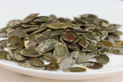 Close-up of pumpkin seeds piled on a white plate.
