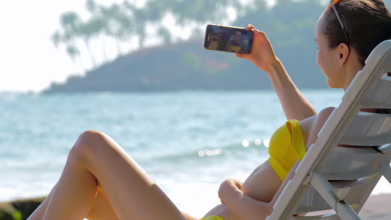 Lady in bikini makes selfie using phone while lying on sunbed