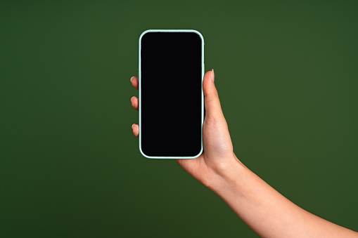 Woman hand holding smart phone with empty screen on green background