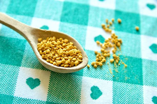 Bee pollen granules crumbled from glass jar n white background. Healthy nutrition.