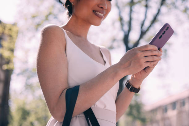 istock Smiling Woman Using Smartphone in Sunlit Urban Setting 2150451622