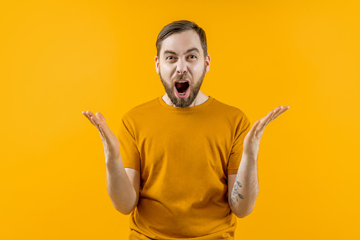 Studio portrait of a young emotional soccer supporter man cheering for his favorite team, isolated over bright colored orange yellow background.