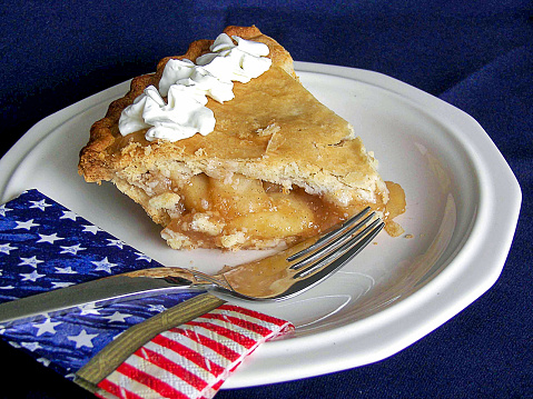 Slice of apple pie with whipped cream garnish and patriotic napkin on a white plate