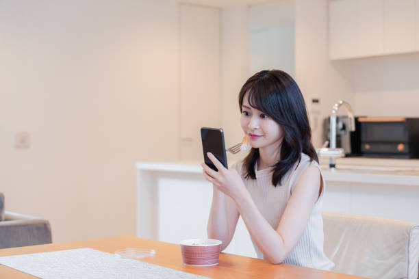 istock Young woman eating dinner at home while using her phone 2150459092