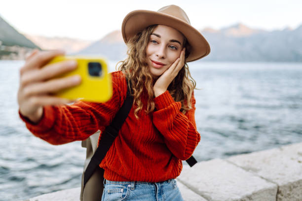 istock Young woman holding mobile phone taking selfie photo using smartphone camera standing on waterfront. 2150459599