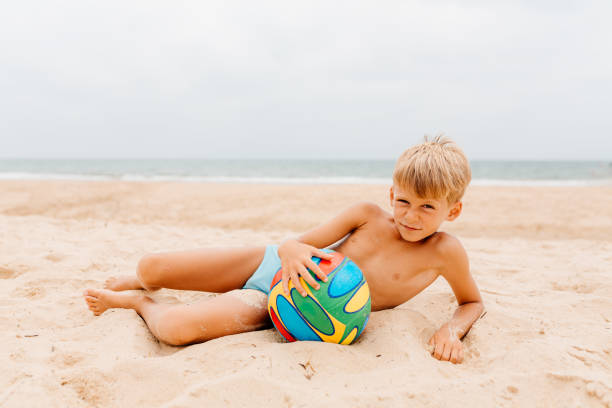 Stock photo showing close-up view of sandy beach with a multicoloured, rainbow striped football by water's edge of sea at low tide in the background. LGBTQ+ gay holiday concept.\n\nStock photo showing close-up view of a pile of seashells with a starfish surrounding a sandstone heart standing up in the sand on a sunny, golden beach with sea at low tide in the background. Romantic holiday and honeymoon concept.\n\n\nClose-up image multicoloured, rainbow striped football on sandy beach, blue, green, yellow, orange and red brightly striped beach toy, sunny sandy beach, waves breaking at low tide, sea and coastline, focus on foreground, lgbtq+ gay holiday concept\n\n\nClose-up image of heart-shape sandstone standing in golden sand, surrounded by heap of seashells, starfish, unrecognisable jogger running on sunny sandy beach, waves breaking at low tide, sea and coastline, focus on foreground, romantic honeymoon concept