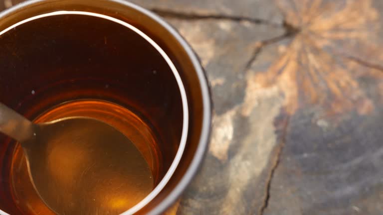 Slowly zooming in on a hot cup of tea on the table: steaming tea spinning by itself. Steam rising from a cup of tea. Tea swirling alone in a cup. Cup of tea, close-up shot, top view. A tea mug on a wooden table. Steamy tea. A tea spoon.