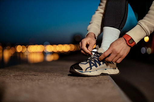 Running Shoes - Closeup of Man Tying Shoe Laces. Male Sport Fitness Runner Getting Ready for Jogging Outdoors at Night. Background With Bokeh Lights
