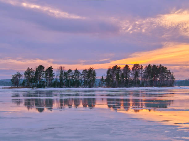 Finnish frozen lake with tree reflections at sunset under dramatic sky.