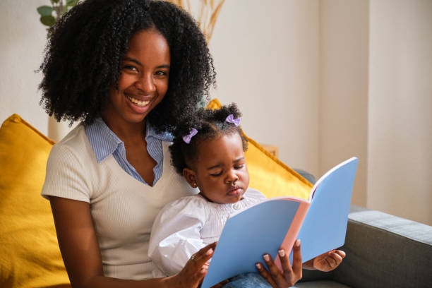 istock A woman is smiling and looking at camera while reading a book to her child. 2150471503
