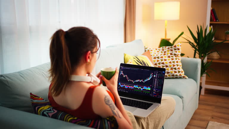 Young Business Woman, sitting on the couch with her feet stretched out, checking the price chart of Bitcoin or stock exchange on a digital exchange on a laptop monitor and cell phone