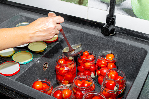Canning tomatoes. A woman pours brine into jars with red ripe tomatoes.