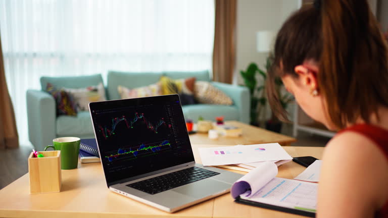 Young Businesswoman checking Bitcoin or stock market price chart on digital exchange on a laptop monitor computer at her desk at home,