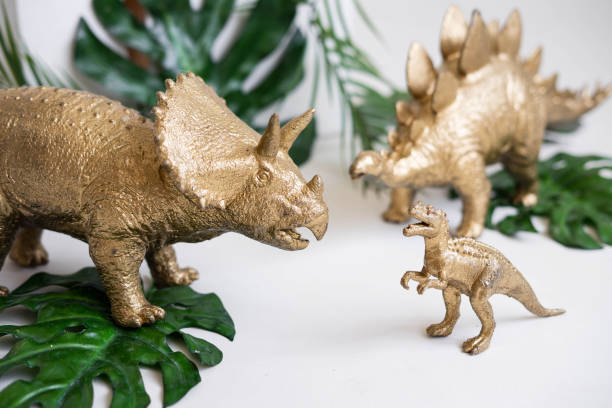istock Golden dinosaur figurines and palm leaves on a white background. 2150493302