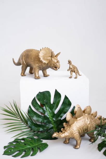 istock Golden dinosaur figurines and palm leaves on a white background. 2150493309
