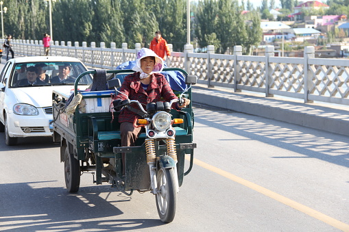 Xinjiang, China - 09/17/2011: A Chinese woman driving a work cargo tricycle on a bridge.