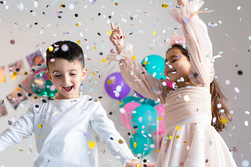 Smiling children with outstretched hands near falling confetti on party background.