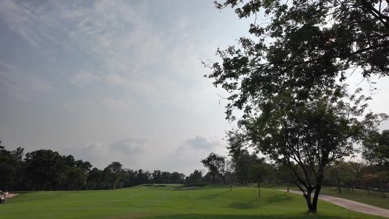 Amidst the beautiful green landscape of a golf course, a corridor of pristine grass weaves its route through the field, while sand bunkers punctuate the terrain. This harmonious blend of sport and health unfolds under the radiant daytime sun.