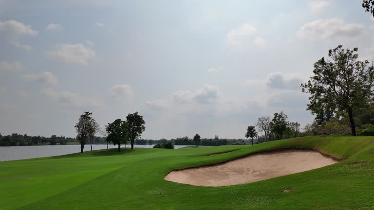 Amidst the beautiful green landscape of a golf course, a corridor of pristine grass weaves its route through the field, while sand bunkers punctuate the terrain. This harmonious blend of sport and health unfolds under the radiant daytime sun.golf course.