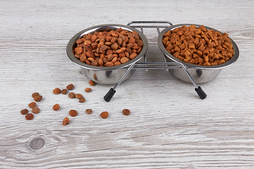 Dry pet food in metal bowl isolated on wooden background