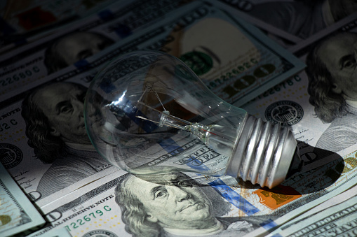 Incandescent lamp lies on dollars in the shade, high price of electricity, business