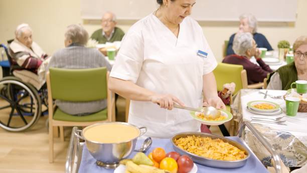 istock Cook serving pasta at seniors sitting in geriatric dinning room 2150513038