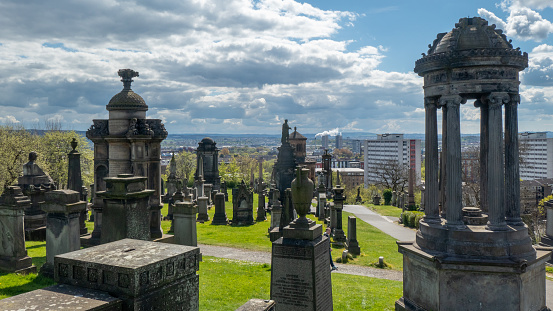 View of Glasgow from the hill of the Necropolis. In the foreground grave monuments of various forms. Sunny weather