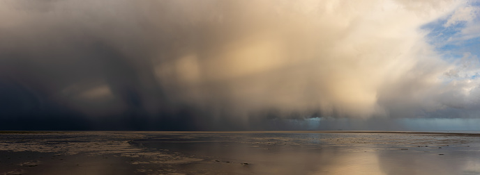 Stunning dramatic stormy skies over ocean panoramic landscape with distant heavy rainfall