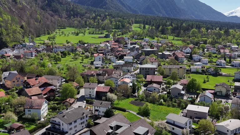 Quaint swiss town with green fields in Trimmis during sunny day. Residential homes and hotels. Aerial forward flight.
