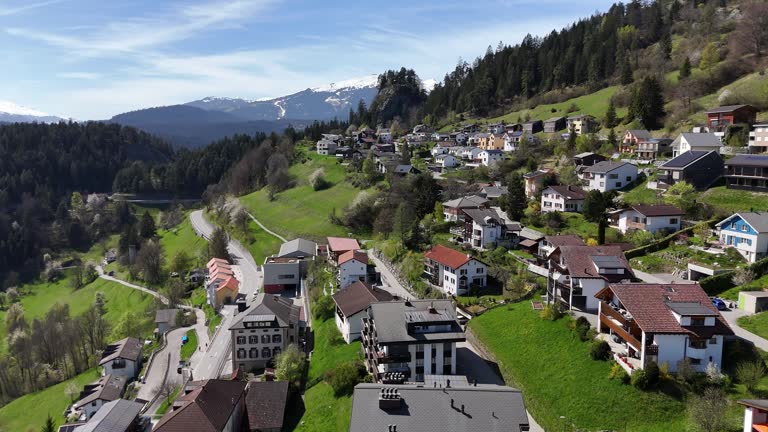 Scenic swiss town with hotel apartments on hill with green pasture and snowy mountains in background. Aerial forward shot.